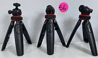 Lot of three compact adjustable tripods with black legs, red rings, and different swivel head styles; photographed upright side by side.