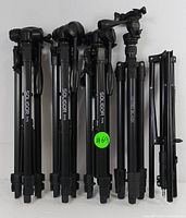 All five items standing upright side by side showing three Soligor tripods, one Optex tripod, and one folded light stand