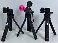 Three compact tripods standing with legs unfolded, showing their adjustable camera mounts and black textured legs.