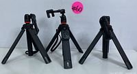 Front view of the three black tripods with different designs and leg arrangements, including one with a wrist strap and smartphone bracket.