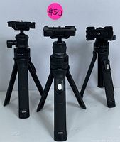 Front view of the three Mobifoto tripods showing their adjustable legs and Bluetooth remote controls with white buttons on handles.