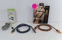 Bundle of three cables: two HDMI cables (one Monster M-Series M2000 braided cable) and one grey Apple USB to Lightning cable laid flat on white surface.