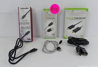 Overview photo displaying three boxed cables and three loose cables: boxed USB Type-C to Type-A cable, DisplayPort to HDMI cable in branded packaging, USB-C to USB-A cable in package, with loose cables including braided USB-C and black USB Type-C cables.