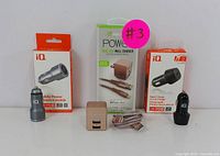 Group photo showing all charging accessories and packaging: beige USB-C dual-port wall charger, braided charging cable, silver and black iQ USB car chargers with boxes.