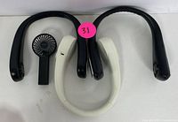 Two portable neck fans, one black and one white, alongside a small black handheld fan laying flat on a white surface.