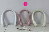 Three neck fans: two white and one pink, displayed front view with two USB cables for charging placed in front.