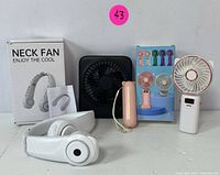 All items shown together: neck fan, black desk fan, pink handheld fan, white handheld fan with digital display, box and manual for neck fan.