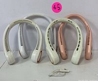 Four USB rechargeable neck fans arranged upright showing curved structure, two in white, one cream, one pink, with a USB cable in front.