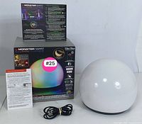 Photo of Monster Smart Illuminessence LED light orb with original packaging, power cable, and instruction manuals displayed on flat surface.