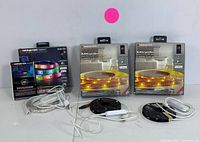 Three Monster Smart Illuminessence LED light strips in original retail packaging with USB power cords and control modules shown on table.