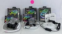 Three boxed and unpacked Monster Smart Illuminessence Neon RGB+IC light strips laid out with power adapters, control units, manuals on white background
