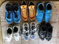 Top down view of six pairs of athletic shoes in various colors arranged in two rows on tiled floor.