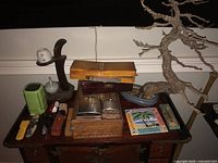 Wide overview of various items on wooden table including wooden boxes, ceramic items on wooden stand, art supplies, flashlights, knives, and battery charger.