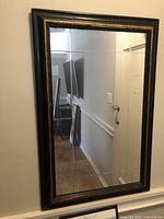Front view of the decorative rectangular mirror showing black frame with gold detailing and segmented mirror panes reflecting hallway.