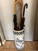 Front view of the ceramic umbrella stand holding three umbrellas with wooden and metal handles.