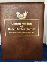 Front cover of the brown leather-bound album with embossed gold text and eagle emblem, displaying the title and 22kt gold proof replica note.