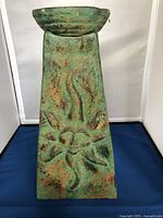 Front view of the green ceramic sun face sculpture showing textured sun face design and rust-colored accents.