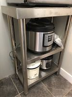 Front angled view of stainless steel kitchen prep table with items on the lower shelves.