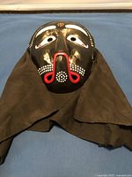Front view of traditional Korean black wooden theater mask with red and white facial patterns and attached black fabric.