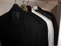 Seven men's blazers and jackets hanging on hangers, showing the variety of colors and materials including black, navy, white, and leather.