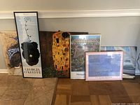 Six framed art and canvas prints arranged on floor, showing variety of sizes, frame styles, and recognizable artwork reproductions
