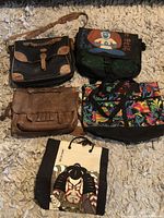 Five bags arranged on carpet showing different styles and materials, including leather and fabric.