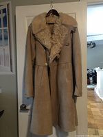 Full view of beige shearling coat hanging on door, showing front design, button closure, pockets, and fur collar.