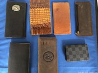 Top-down view of seven men's wallets showing different textures, colors, and styles spread on a blue fabric