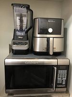 Photo showing Ninja blender, Instant air fryer, and Cuisinart microwave oven stacked on a shelf.