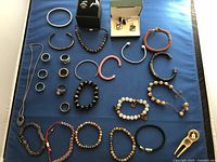 Full view of multi-piece jewelry laid out on blue cloth including rings, bracelets, necklace, cufflinks, and golf divot tool
