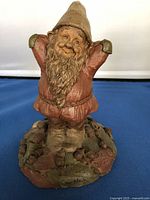 Frontal view of a multicolored gnome figurine with a long beard, pointed hat, and raised arms on textured base showing artist signature and name 'Miles'.