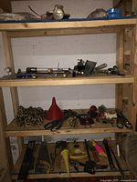 Wooden shelves containing various hand tools including chisel set, caulking gun, vice, funnel, chains, and a floor jack below.