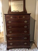 Front view of mahogany tallboy dresser with brass handles and large mirror, showing all seven drawers closed.