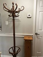 Coat rack and wooden pedestal set placed against a wall and viewed from a distance to show full height