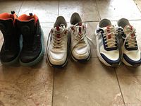 All three pairs of men's sneakers arranged side by side on a tiled floor: Under Armour on left, GDefy middle, J. Lindeberg right.