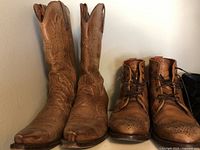Photo showing tall brown cowboy boots with decorative stitching next to brown leather lace-up boots with brogue detailing