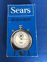Blue original Sears box with printed stopwatch image and branding, showing wear and scuff marks.