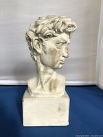 Side view of white plaster bust sculpture showing detailed curls and profile of David's face with slight discoloration and wear marks.
