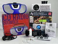 Photo of all items in the lot including the RCA projector with its box, Proscan CD radio boombox with box, Bluetooth smartwatch with charging accessories and manuals.