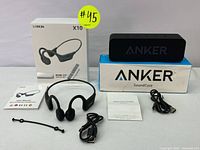 Photo showing Anker SoundCore speaker placed on its box, Lobkin X10 headphones, USB cables, and user manuals with packaging for headphones visible