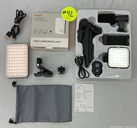 Top view of full video conference light set showing LED panel, clamp mount, wireless remote, USB cable, soft gray pouch, user manual, and box.