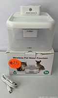Full view of wireless pet water fountain on box, showing water level markings and included USB charging cable.