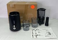 Full view of juicer components laid out with original box, showing main motor unit, juice and pulp containers, plunger, and manuals.