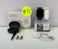 Full lot including packaged hearing amplifier, hearing amplifier charging case with earbuds, ear tips, cleaning brush, Bluetooth smart watch on stand, and charger cable.