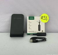 Black fast wireless charging stand and UGREEN branded Bluetooth audio transmitter/receiver with USB cable and box shown upright.