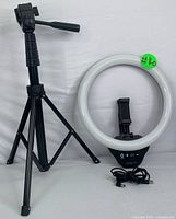 Photo showing LED ring light with USB cable and brightness controls, black phone holder and adjustable tripod stand with pan handle.