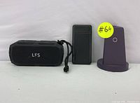 Photo showing all three items: black LFS portable Bluetooth speaker, black rectangular power bank, and purple wireless charging stand with charging circle.