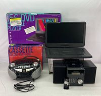All three items together with their original packaging visible behind, showing the Proscan Elite DVD player open and powered off, Cassette/CD/FM Radio and Stereo System positioned in front.