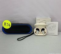 Portable Bluetooth speaker with black mesh and blue trim, black carrying strap visible, and white true wireless earbuds in charging case next to retail box and user guide.