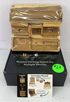 Front view of the wooden docking station still in plastic wrapping on top of the product box with label and instruction manual.